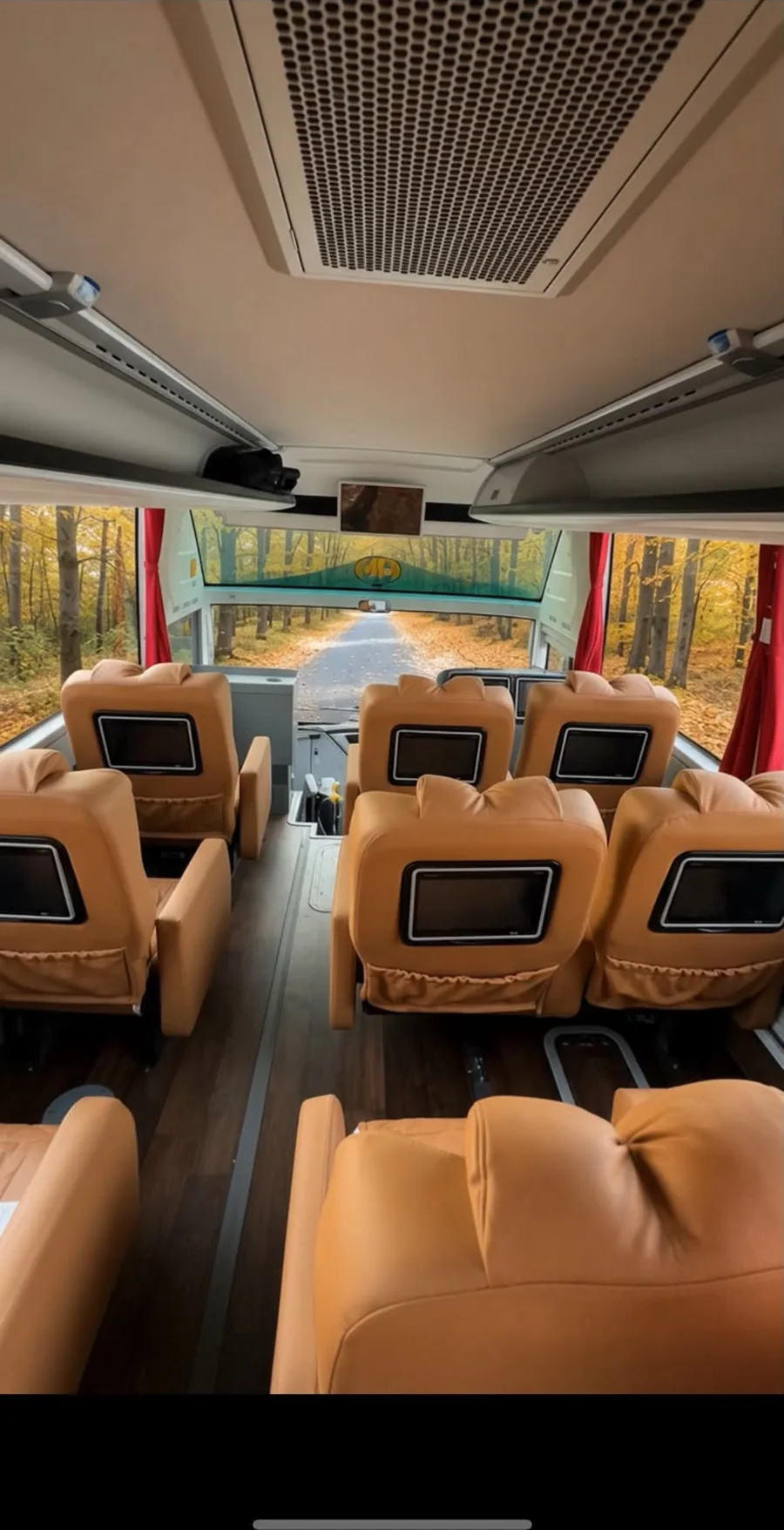 The front of a Premium Plus coach: tan leather sofa seats in a two-plus-one layout with screens in the seat backs